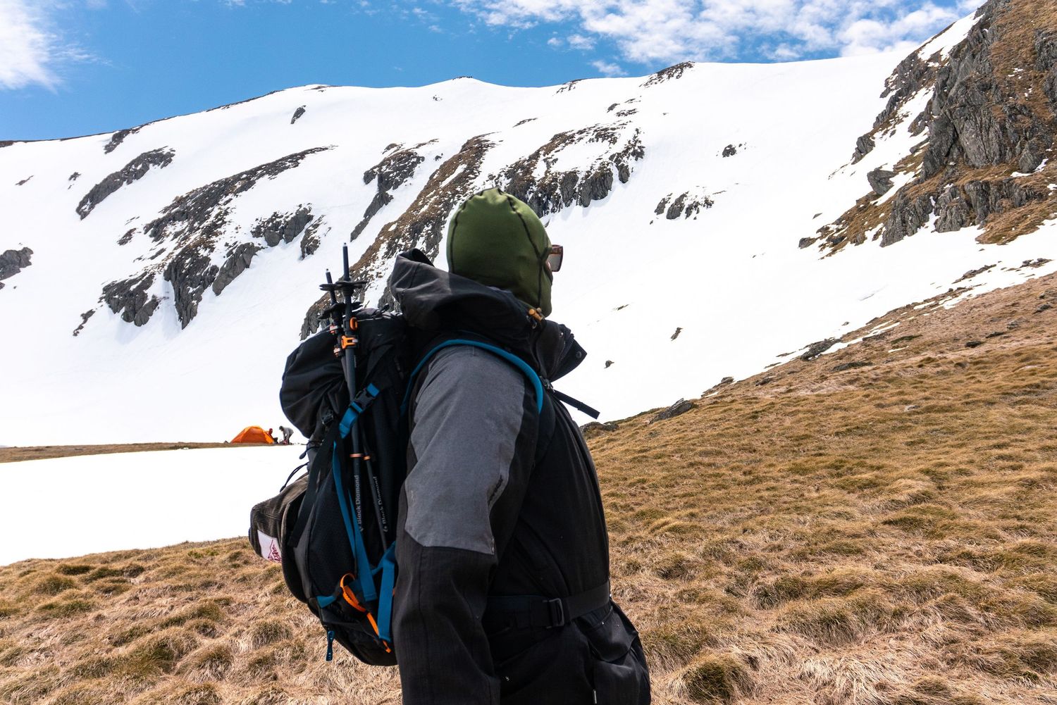 Hiker with backpack trekking toward snow-capped mountain under blue sky.