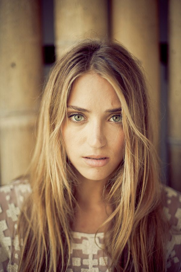 Close-up portrait of a young woman with long blonde hair and green eyes wearing a patterned top.