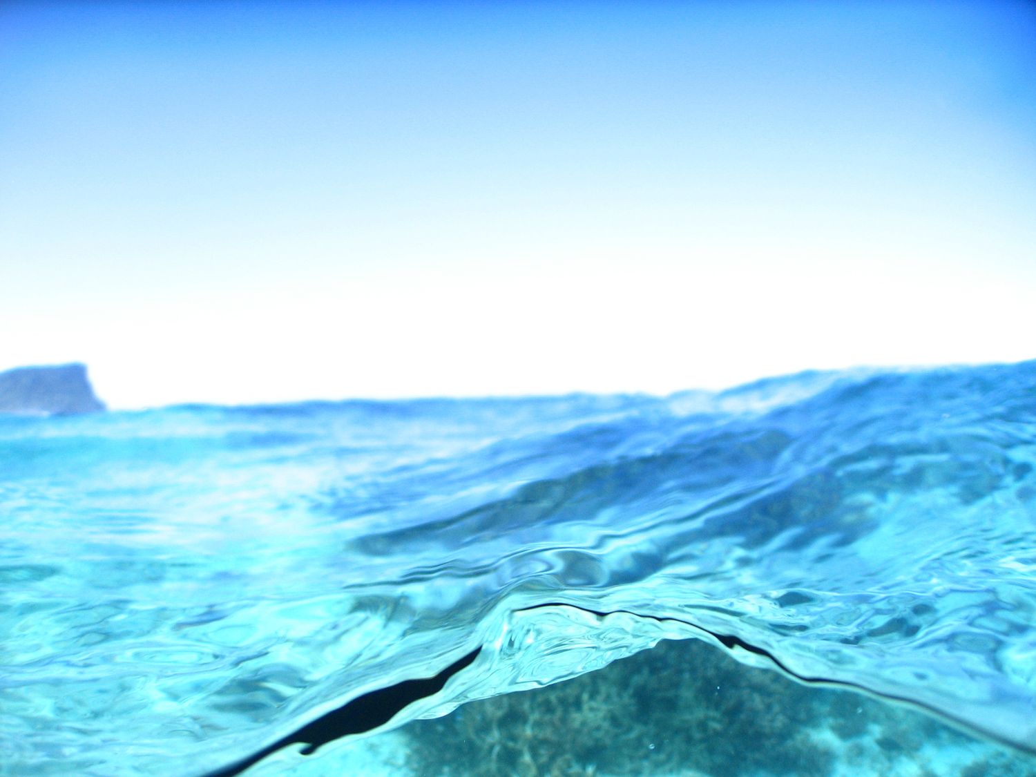 A serene split-level ocean view shows calm turquoise waters with a rocky island on the horizon.