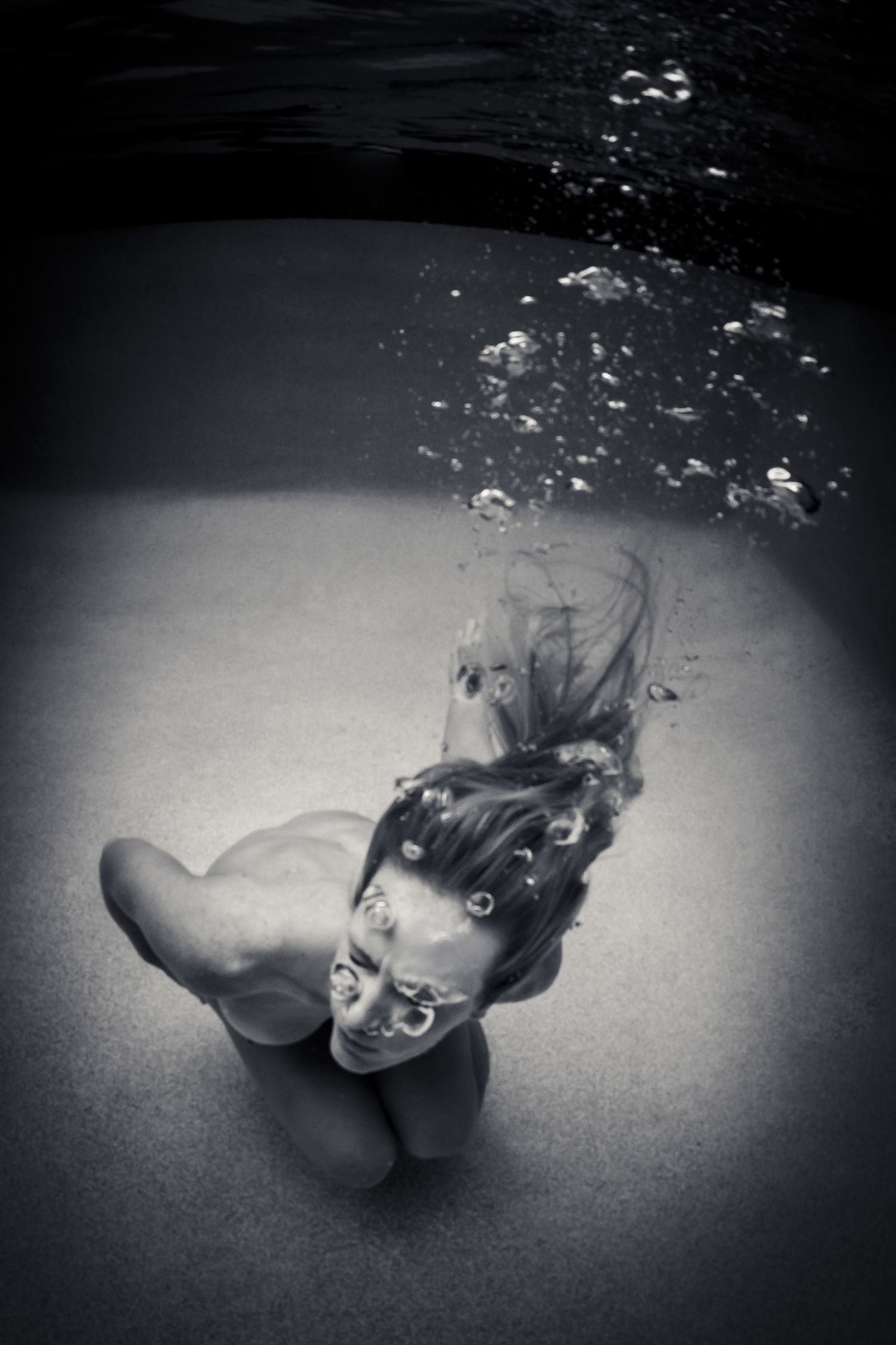 Black and white underwater photo of woman sinking with hair flowing and bubbles rising.