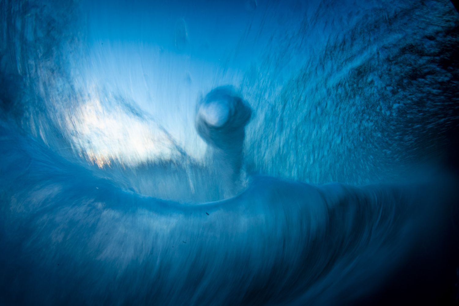 Underwater blue wave photography with surfer silhouette inside barrel.