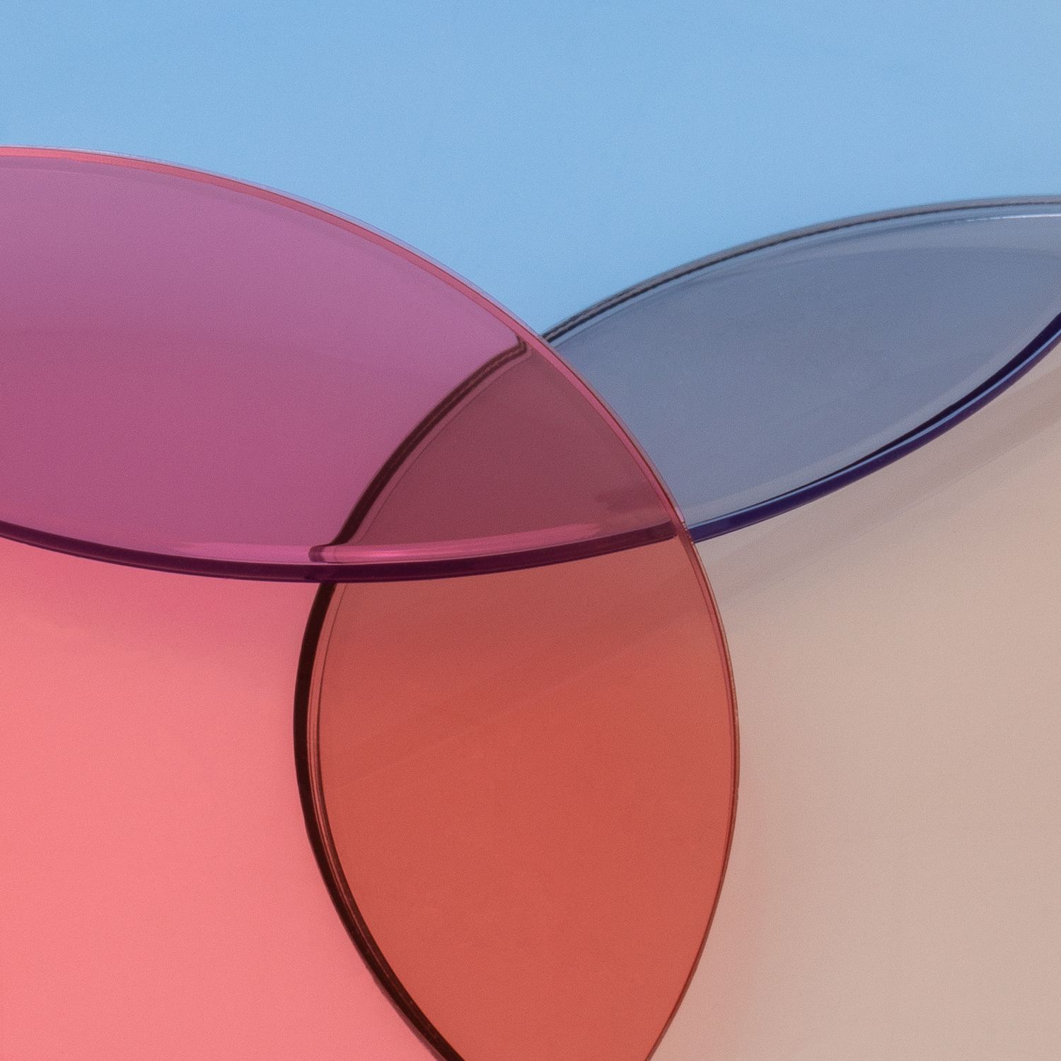 Three overlapping translucent colored glass circles in pink, purple, and peach on a blue background.