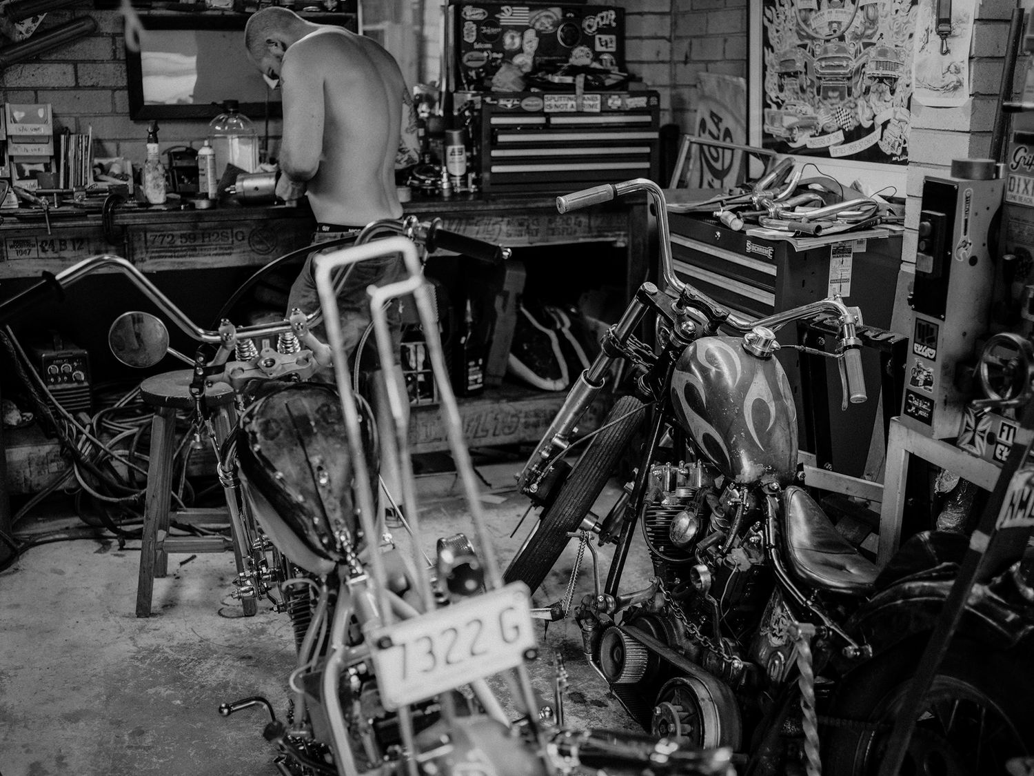 Black and white photo of custom chopper motorcycles in a mechanic garage.