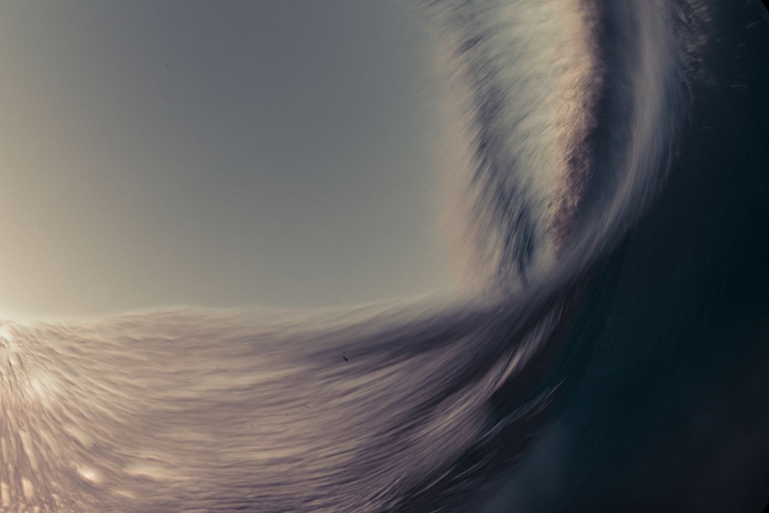 Close-up of a large ocean wave curling with sunlight glowing through the mist.