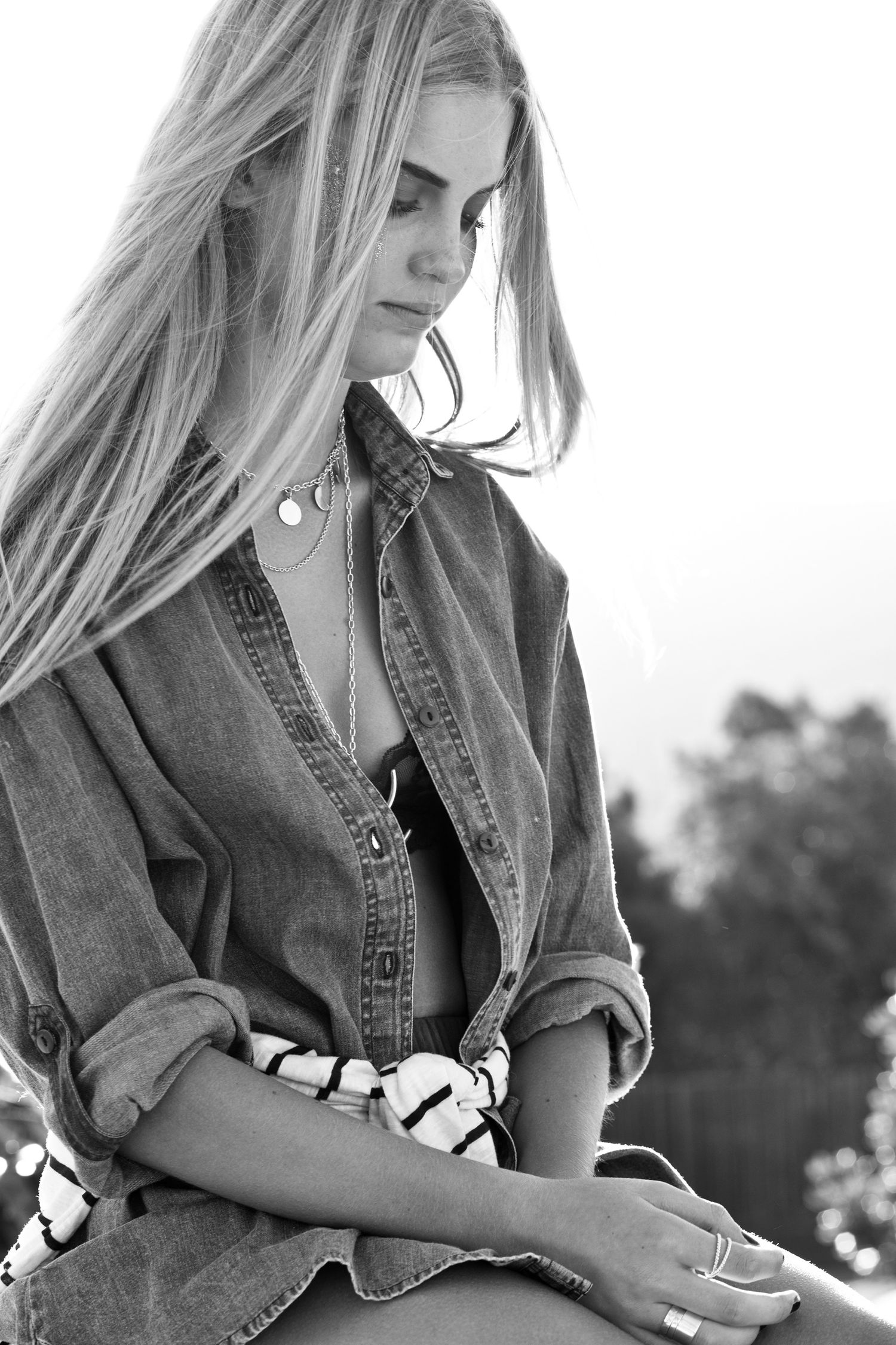 Black and white photo of blonde woman in denim shirt sitting outdoors.