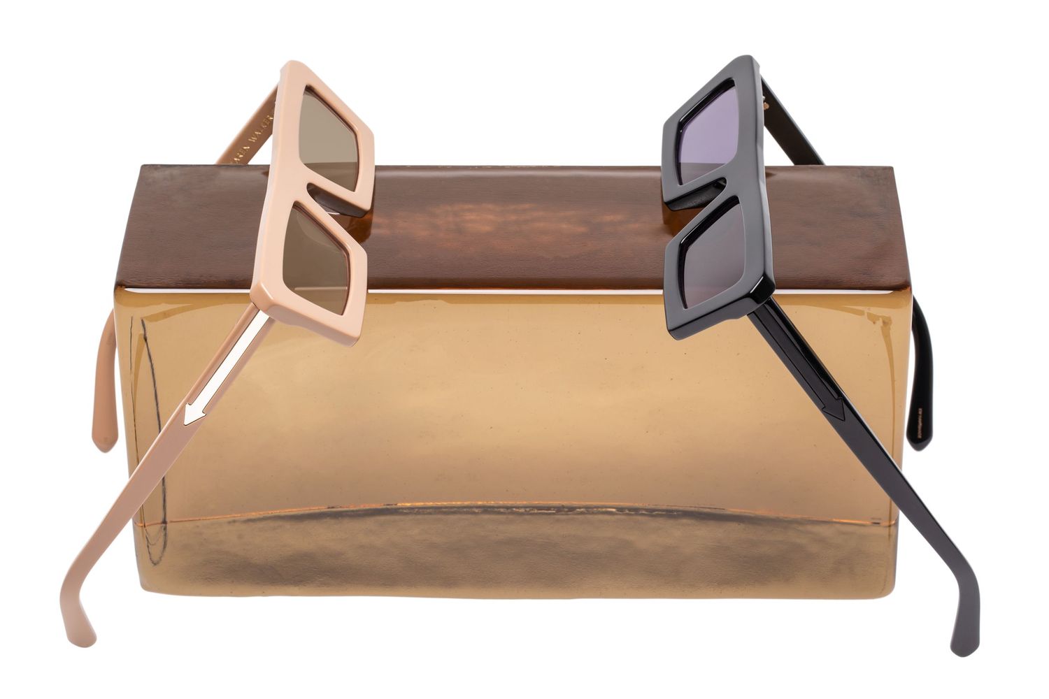 Two geometric square-frame sunglasses in pink and grey leaning on a gold clutch bag.