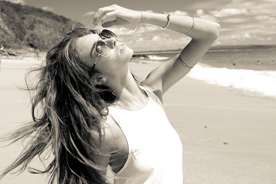 Black and white photo of woman with sunglasses enjoying beach breeze.