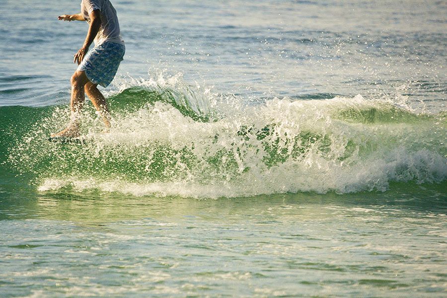 Surfer riding a small green wave in shallow ocean water on a sunny day.