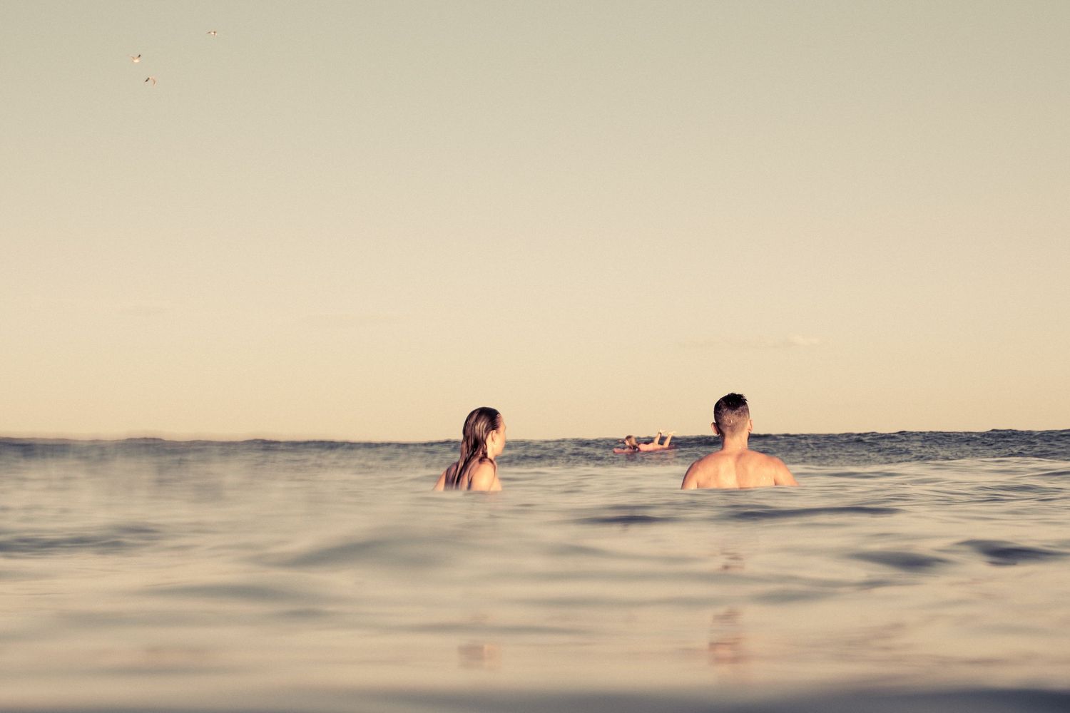 Two people swimming in calm ocean water at golden sunset hour.