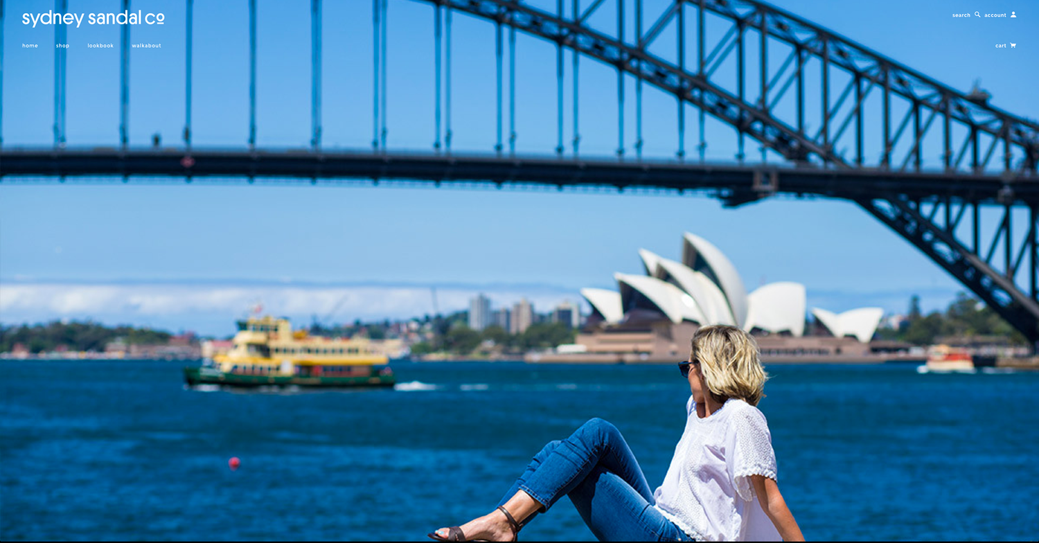 Blonde woman sitting by Sydney Harbour with iconic Opera House and Harbour Bridge in background.