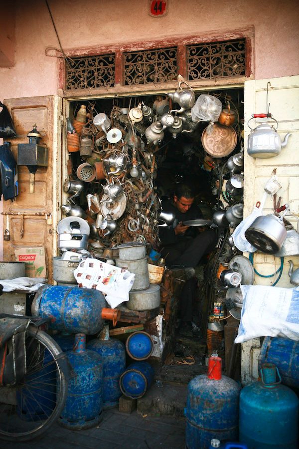 A cluttered Moroccan market stall overflowing with metal pots, kettles, and blue gas canisters outside.