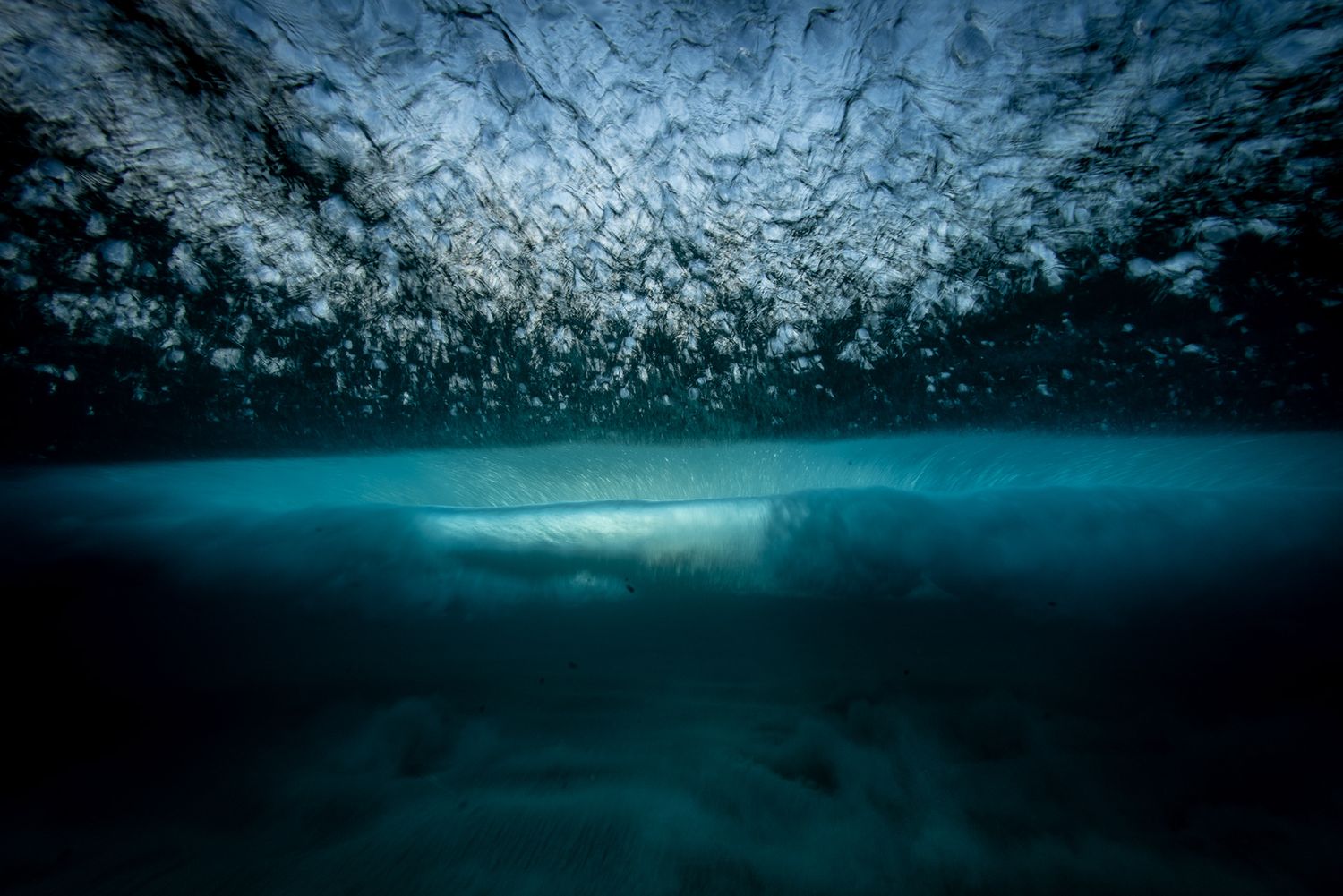 Dramatic underwater view of ocean waves with light filtering through the surface.