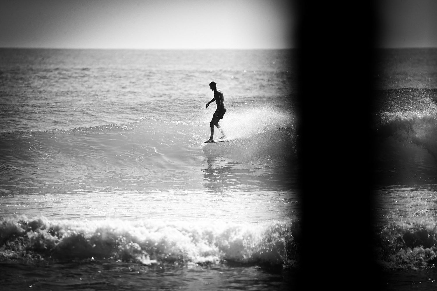 A lone surfer rides a wave in black and white ocean photography.