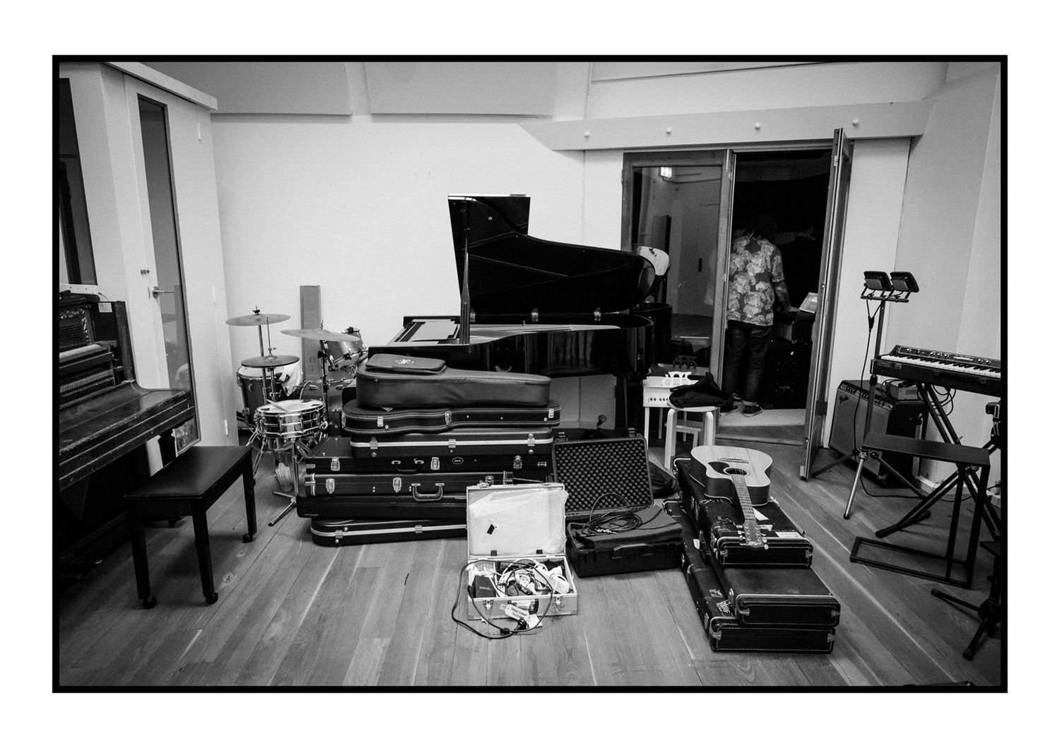 Black and white photo of a music studio with grand piano and instrument cases on floor.