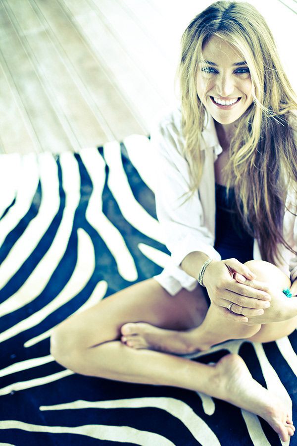 Smiling blonde woman sitting cross-legged on zebra print surface wearing white blazer.