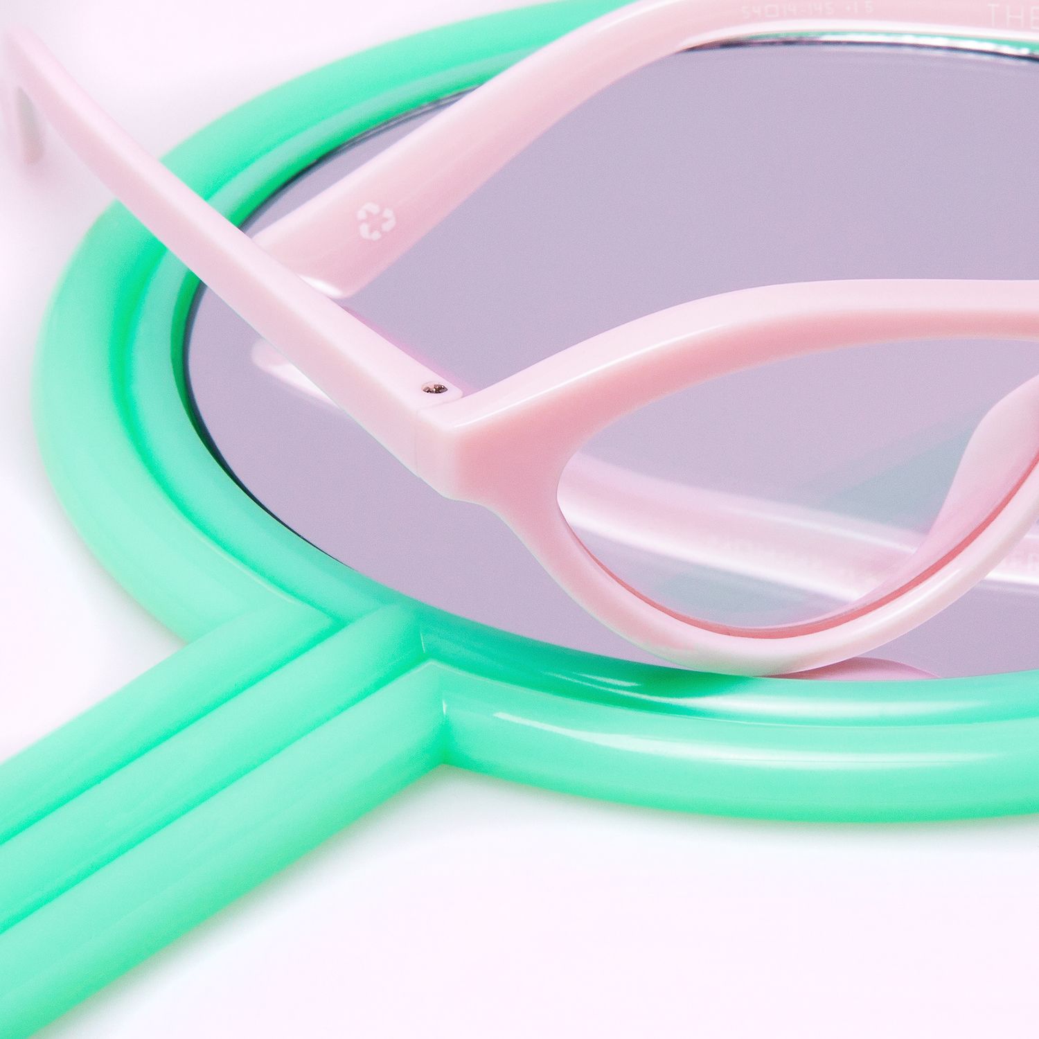 Pink cat-eye sunglasses resting on a mint green hand mirror with reflective surface.