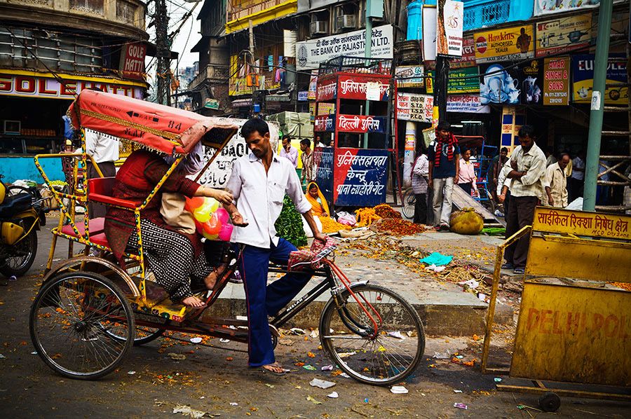 Cycle rickshaw driver standing beside loaded rickshaw on busy Indian street market.