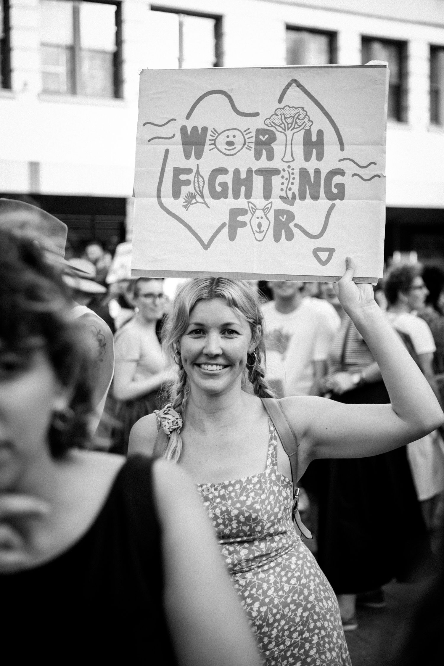 Smiling woman holding a cardboard protest sign reading Worth Fighting For at an outdoor rally.