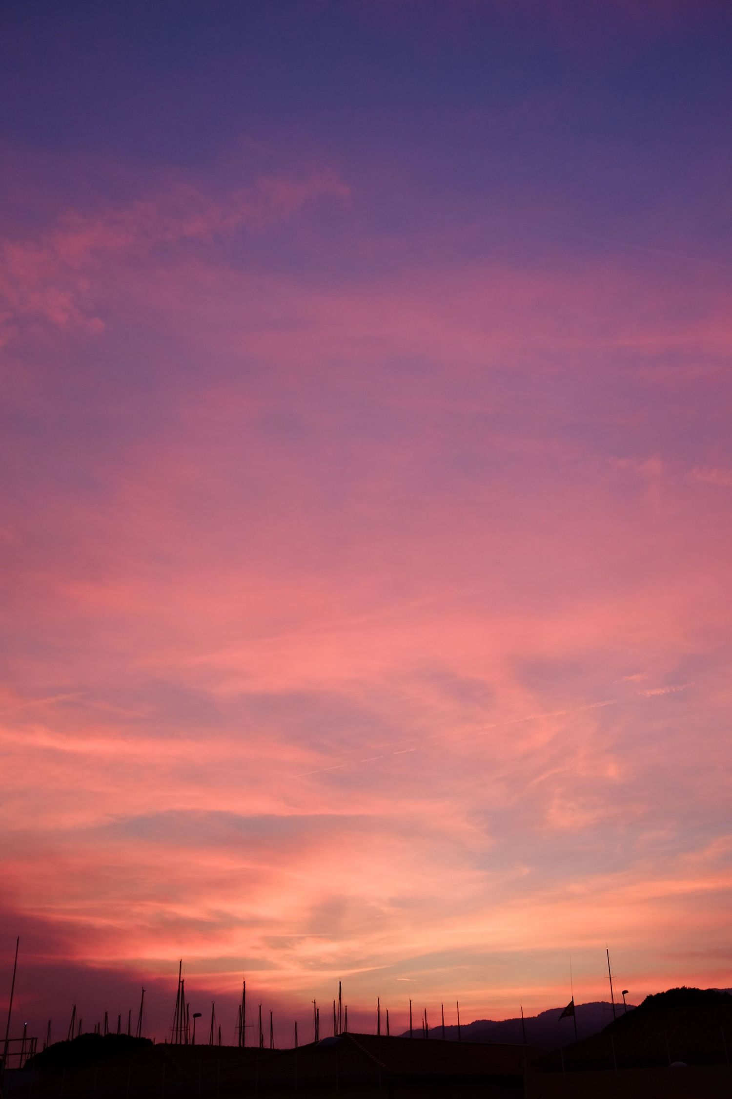 Stunning vibrant pink and purple sunset sky with wispy clouds over silhouetted hilltop antennas.