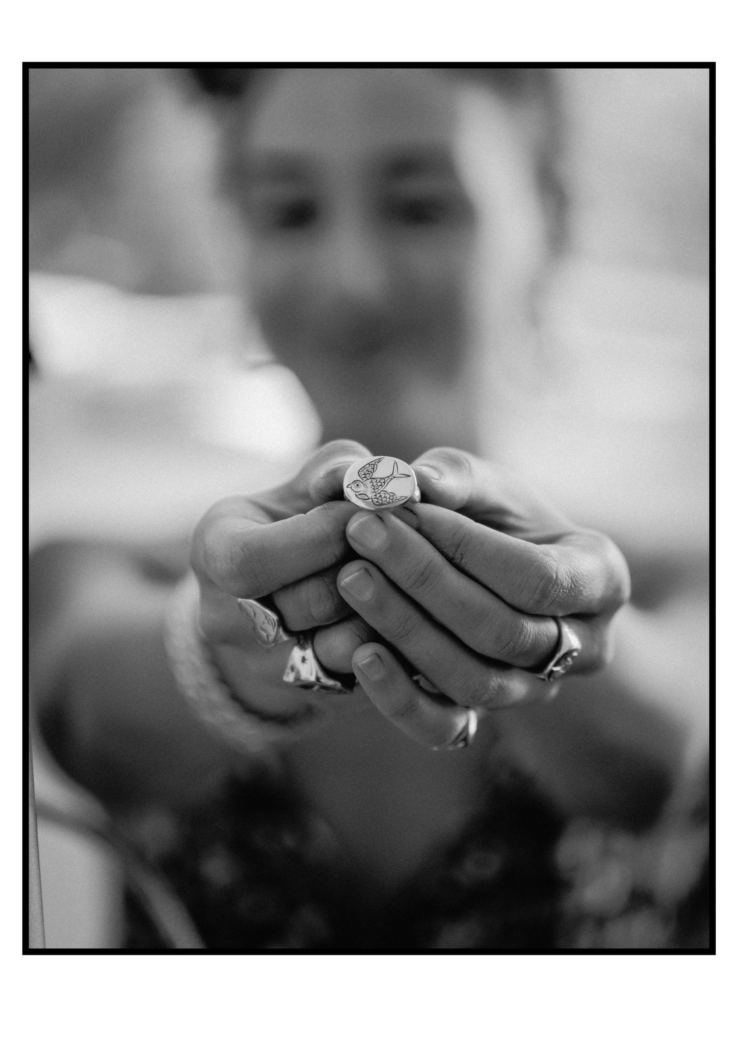 Person holds small ornate coin or medallion toward camera in close-up black and white photograph.