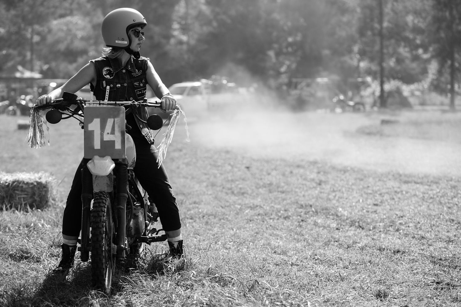 Black and white photo of a motocross rider on bike number 14 in a dusty field.
