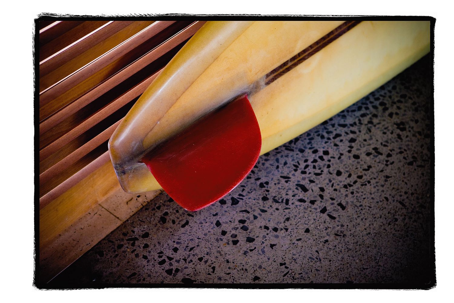 Close-up of a yellow surfboard with red fin detail on a speckled floor.