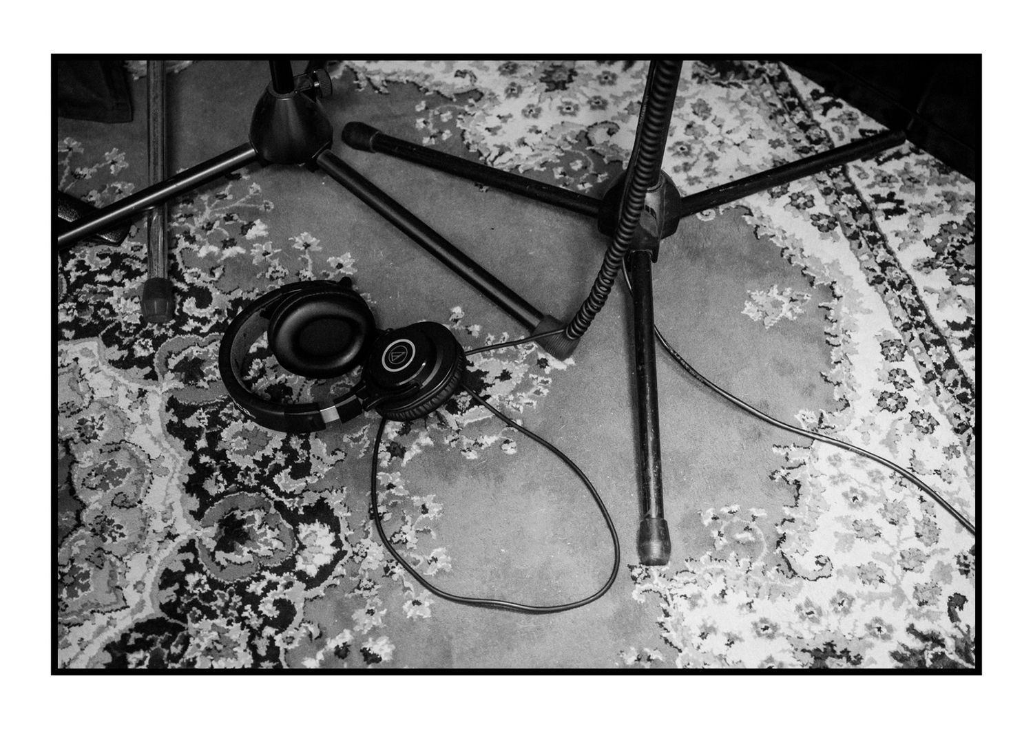 Black and white photo of headphones and microphone stand on patterned rug.