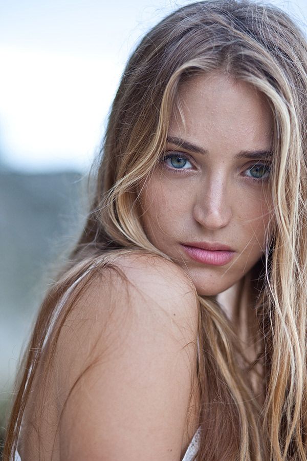 Close-up portrait of a young woman with blue eyes, freckles, and long blonde highlighted hair.