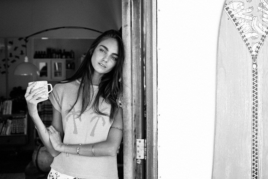 Black and white photo of a young woman leaning against a doorway holding a coffee mug.