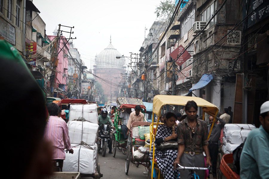 Busy crowded street in Old Delhi India with cycle rickshaws and mosque dome visible.
