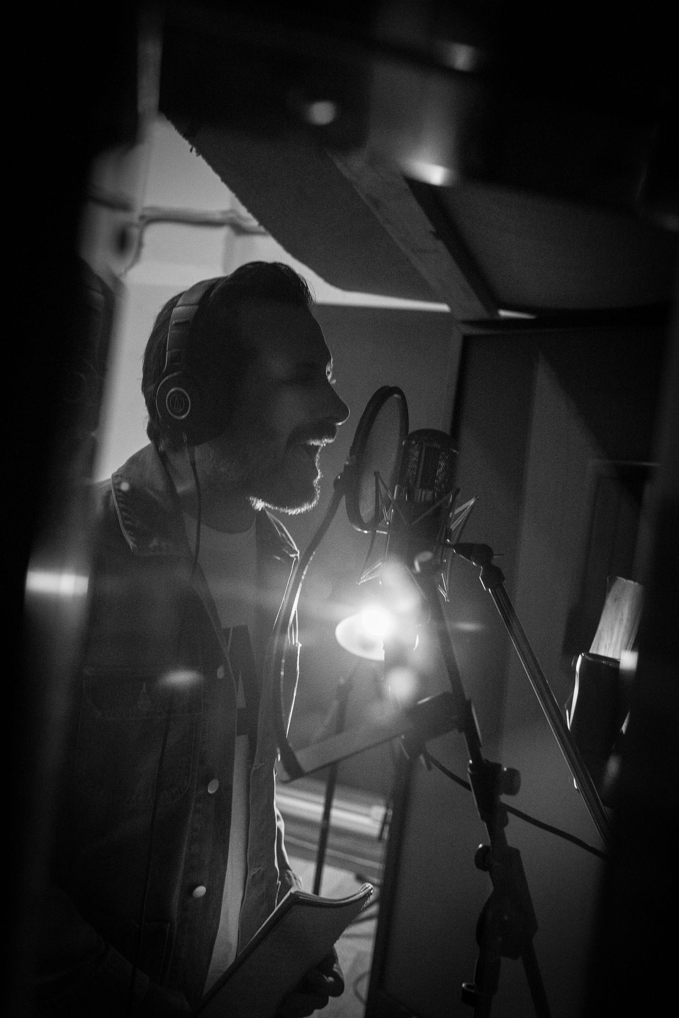 Black and white photo of male vocalist recording in professional music studio with condenser mic.