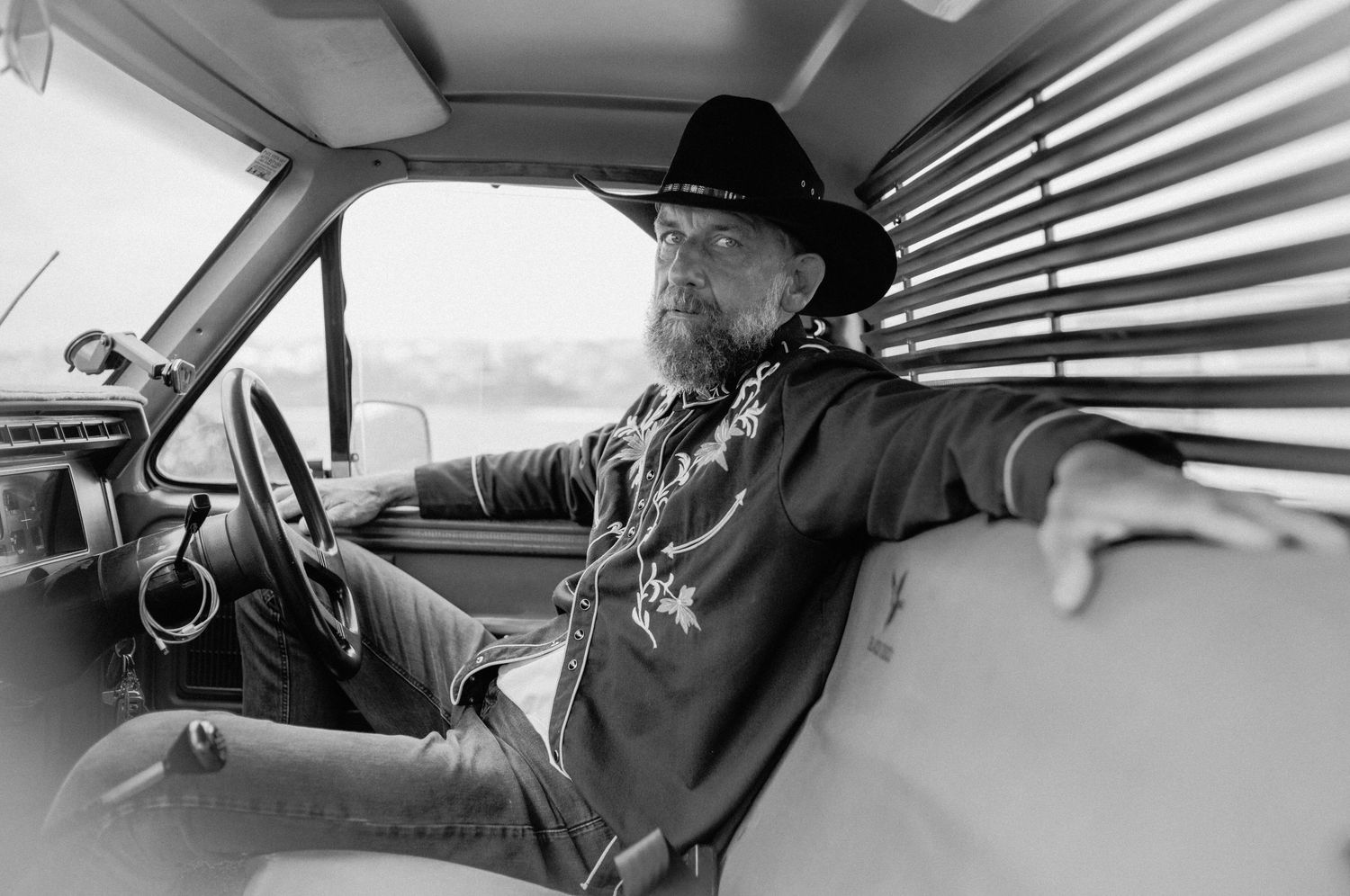 Man in black cowboy hat sitting in vintage truck cab, black and white photo.