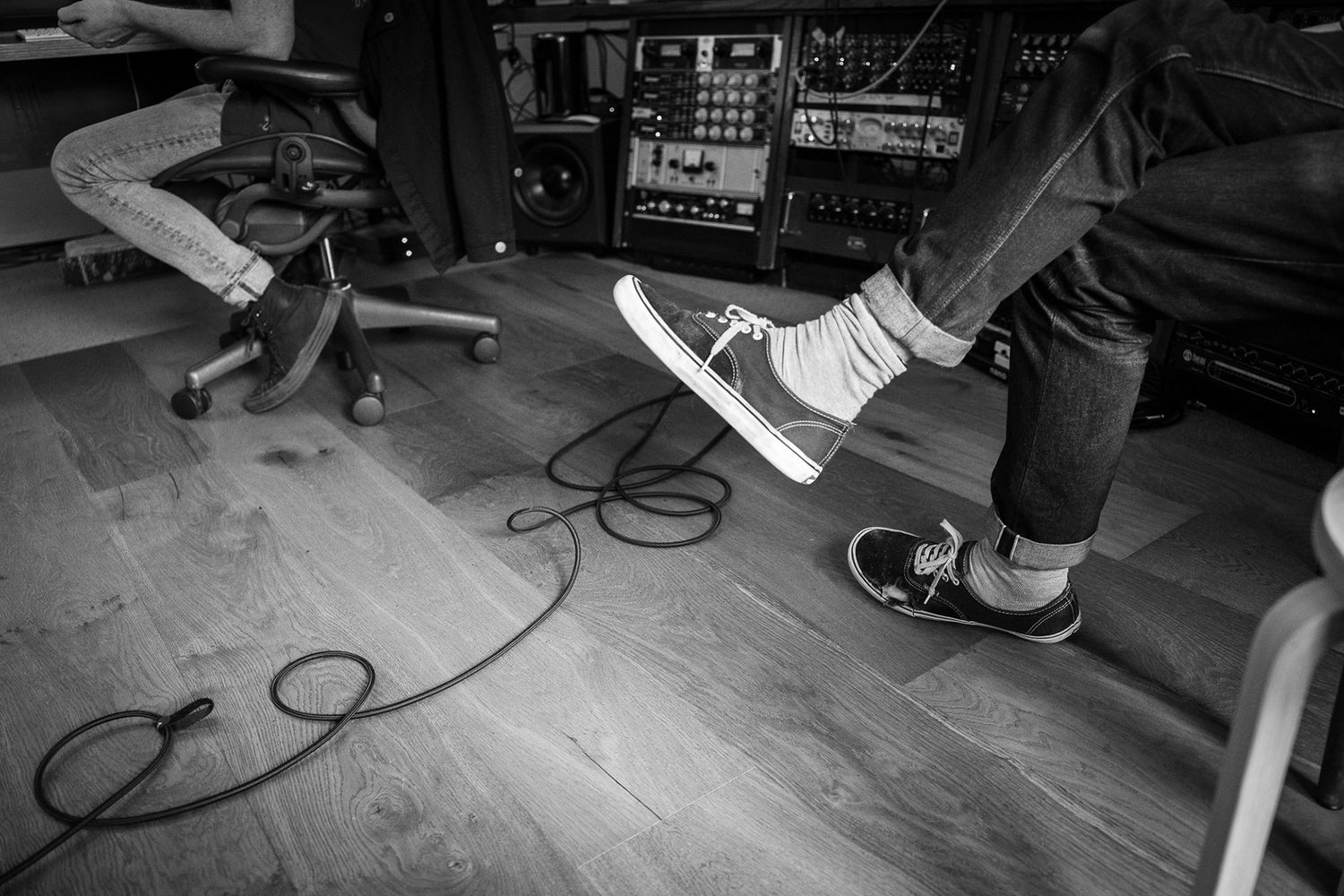 Black and white photo of two people sitting in a music studio with Vans sneakers visible.