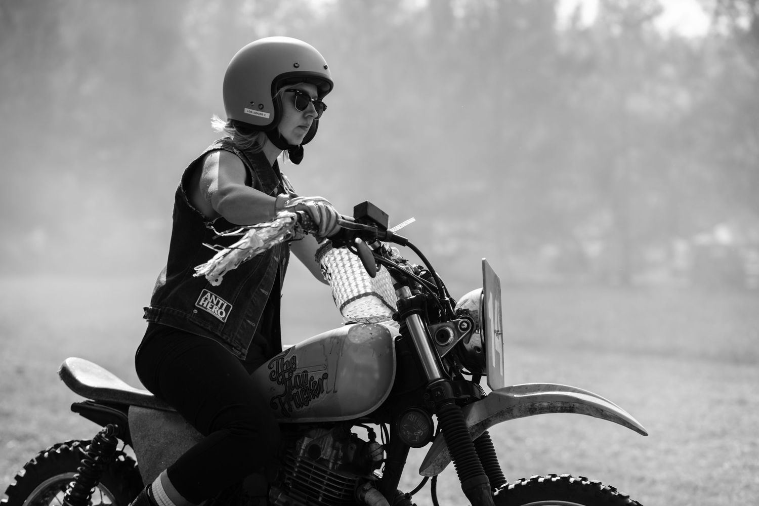 Woman in helmet riding a dirt motorcycle in black and white photography.