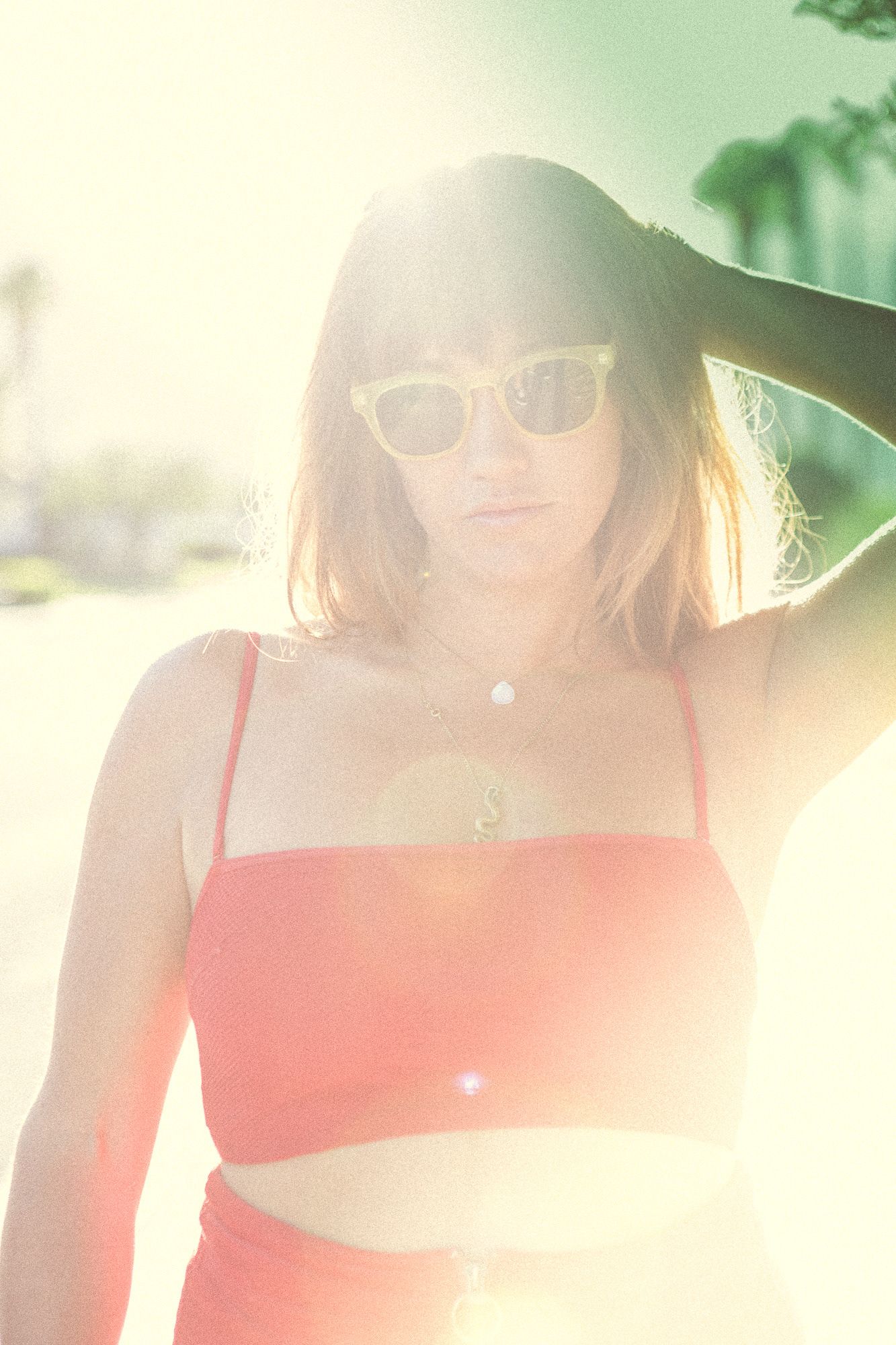 Young woman in pink bikini top and sunglasses posing in bright sunlight.