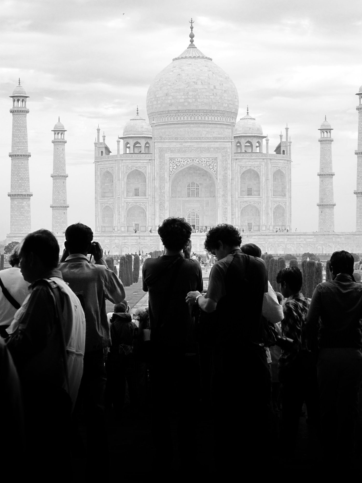 Black and white photo of tourists silhouetted against the iconic Taj Mahal in Agra, India.