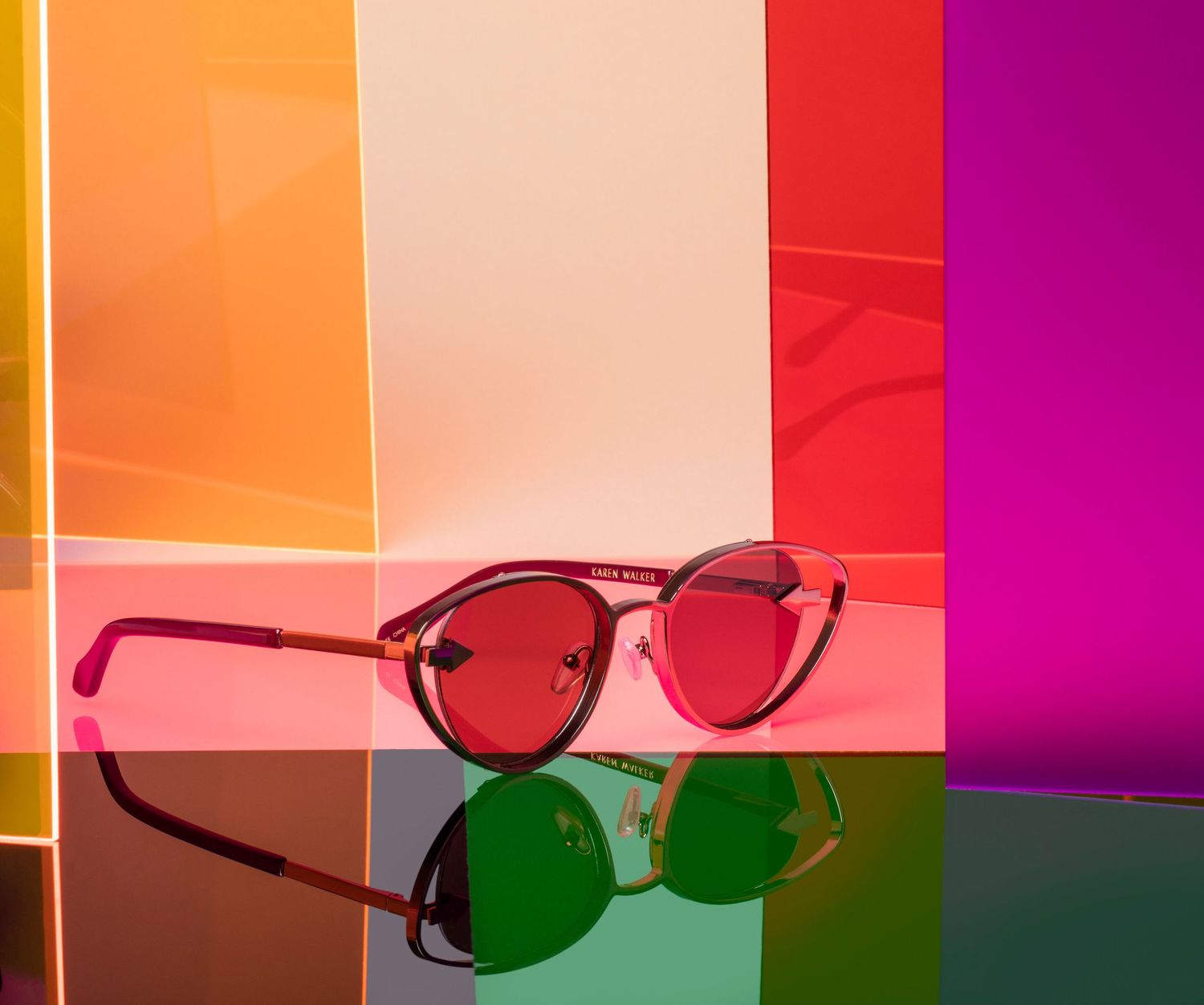 Trendy round red lens sunglasses displayed against vibrant colorful rainbow transparent panels background.