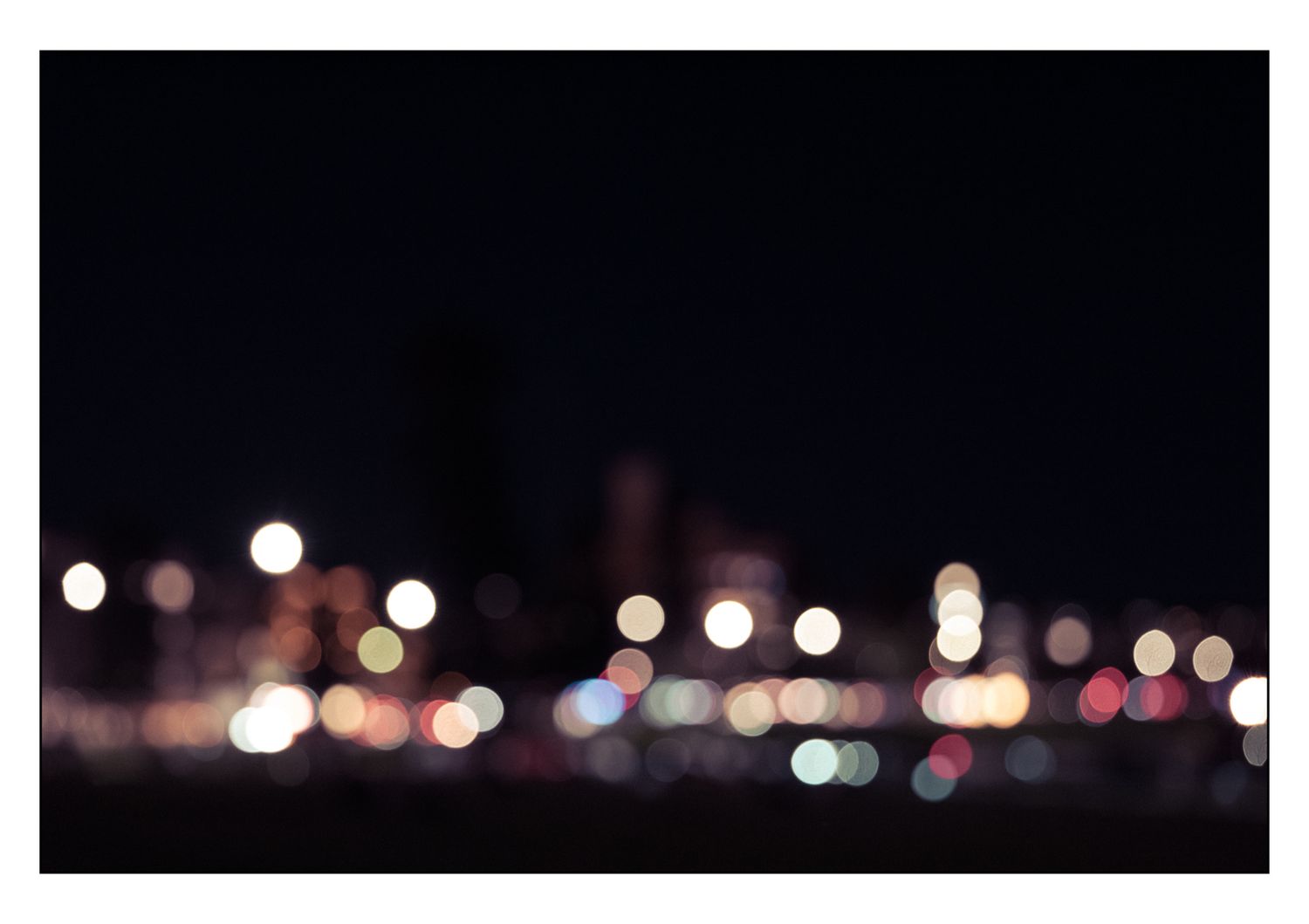 Blurred bokeh cityscape at night with colorful glowing lights against a dark sky.