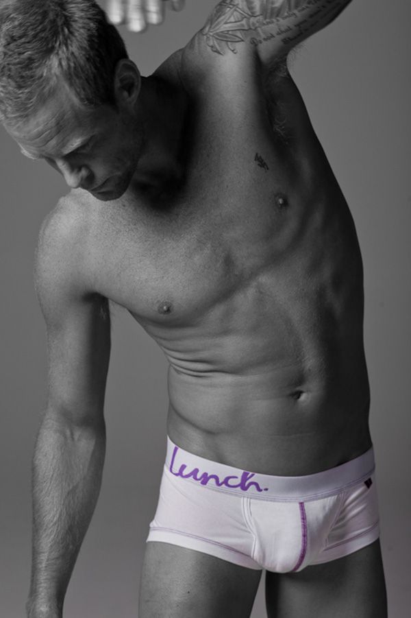 Black and white photo of athletic man posing in white Lunch brand boxer briefs.