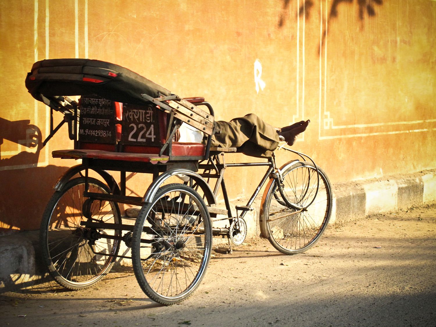 Vintage cycle rickshaw number 224 parked against a weathered yellow wall on a dusty street in India.