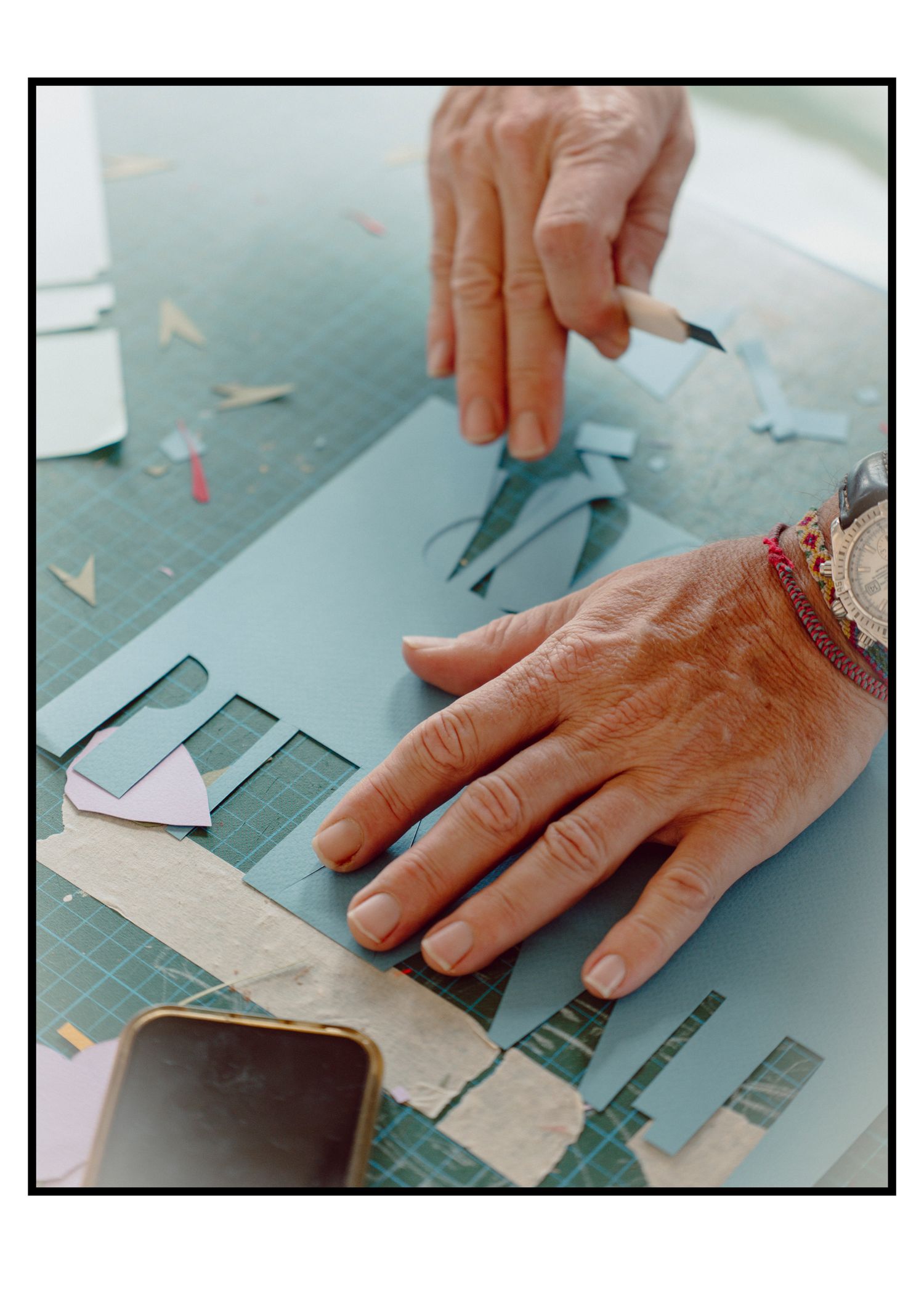 Close-up of aged hands cutting and arranging paper pieces in a collage artwork.