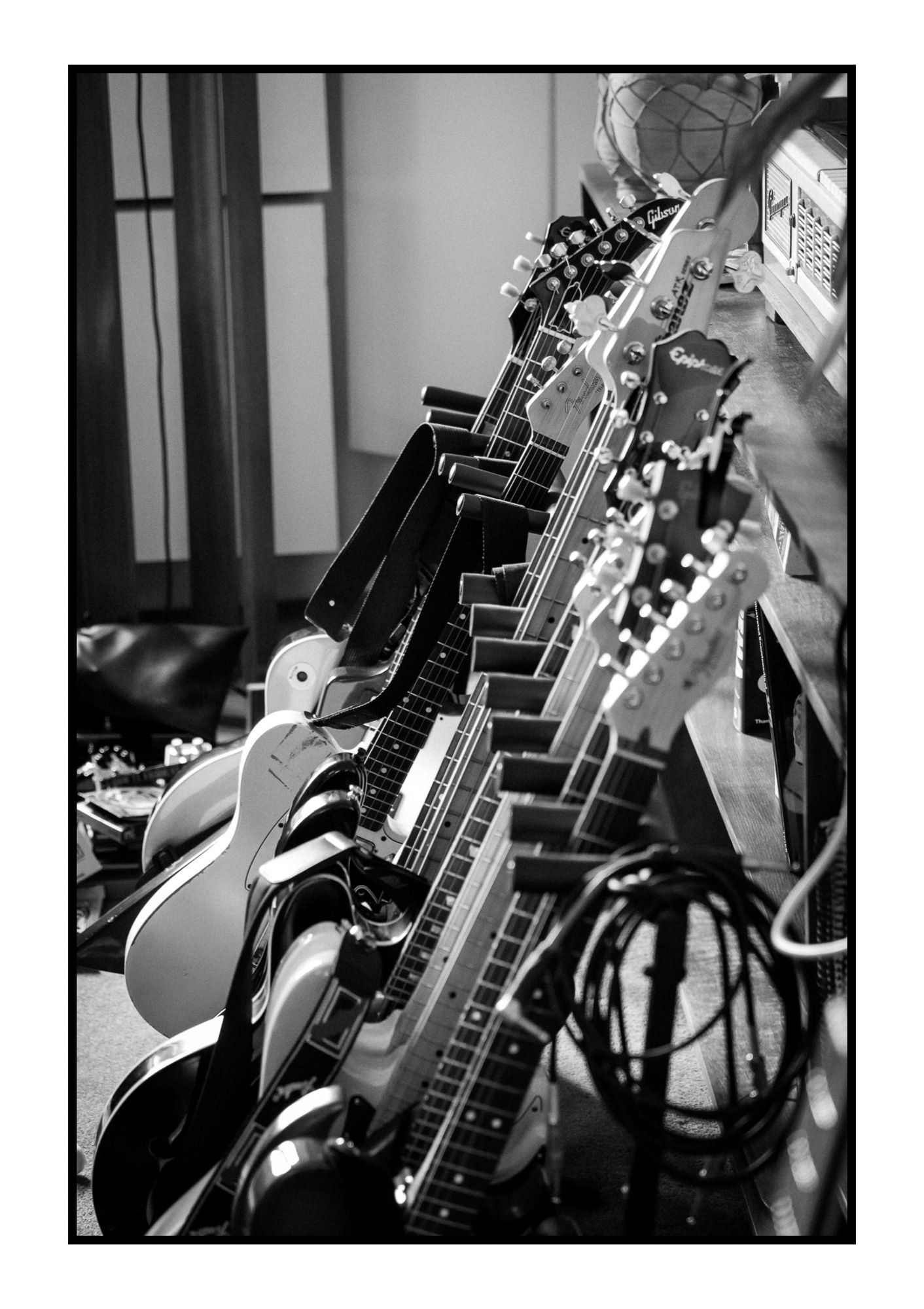 Black and white photo of multiple electric guitars lined up in a row in a music store.