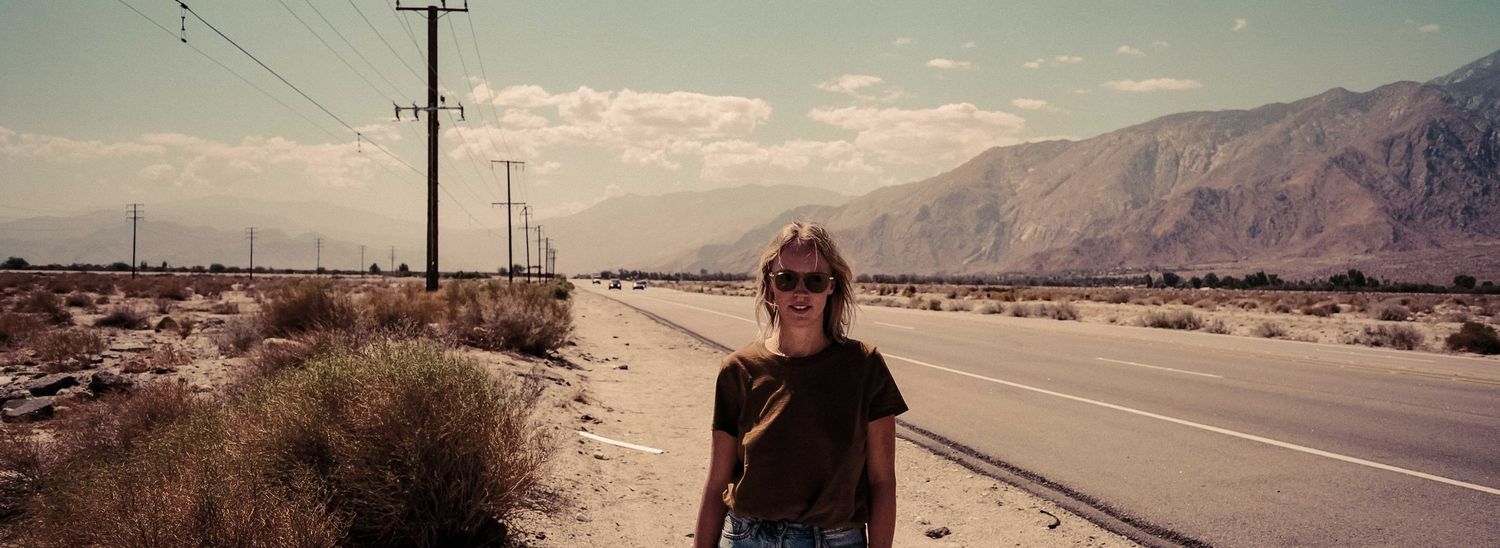 Woman standing on desert highway with mountains in background vintage photo.