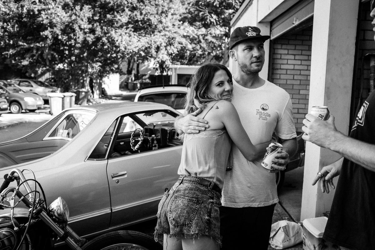 Black and white photo of a couple embracing outdoors near a classic car.