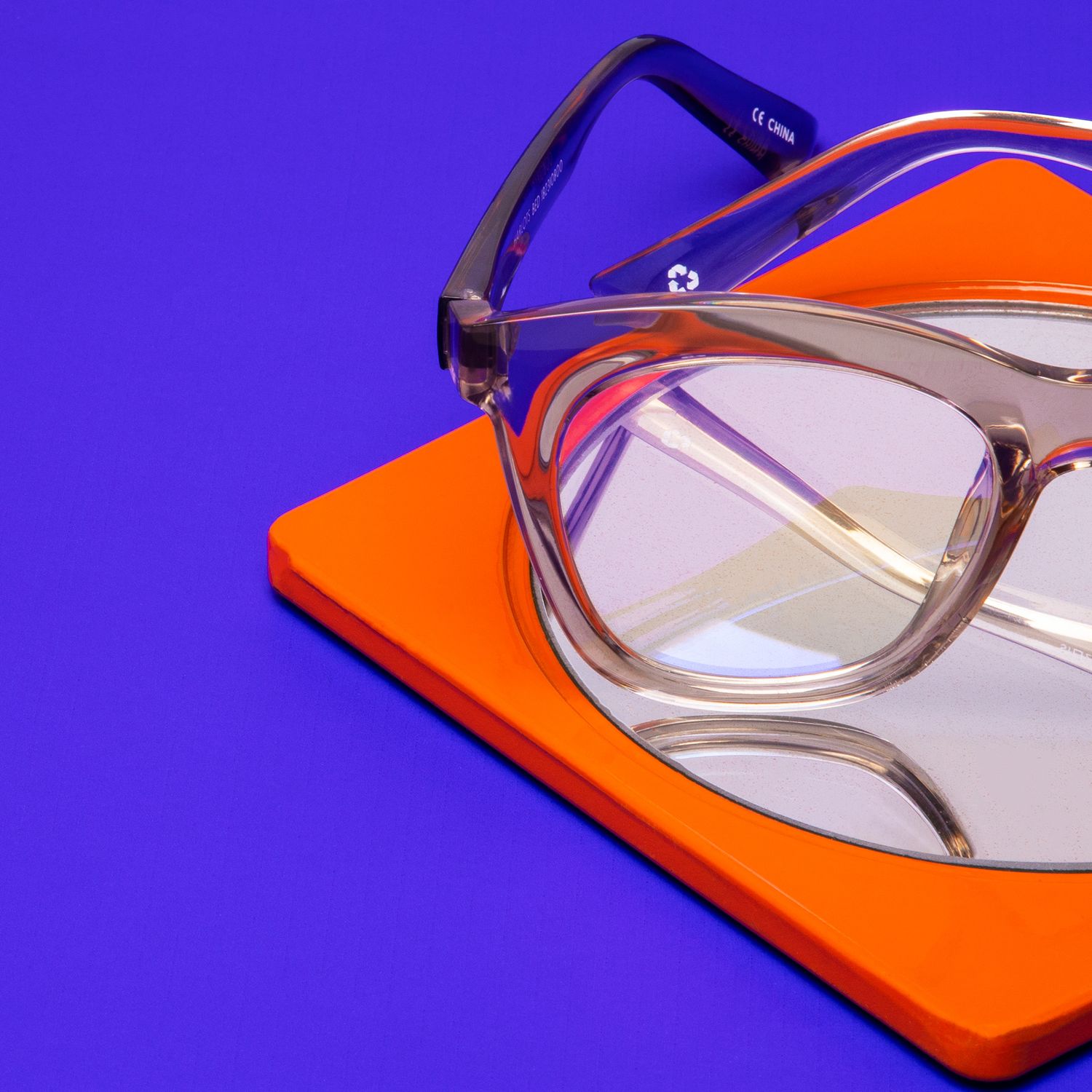 Clear transparent taupe cat-eye eyeglasses on orange book against vibrant purple background.