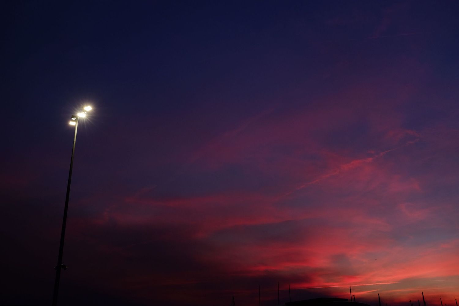 A dramatic twilight sky with vibrant pink and purple clouds behind a illuminated sports field light pole.