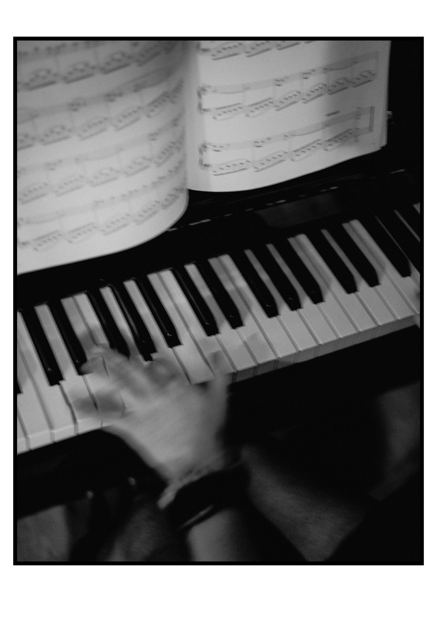 Close-up black and white photo of hands playing piano with sheet music open on stand above keys.