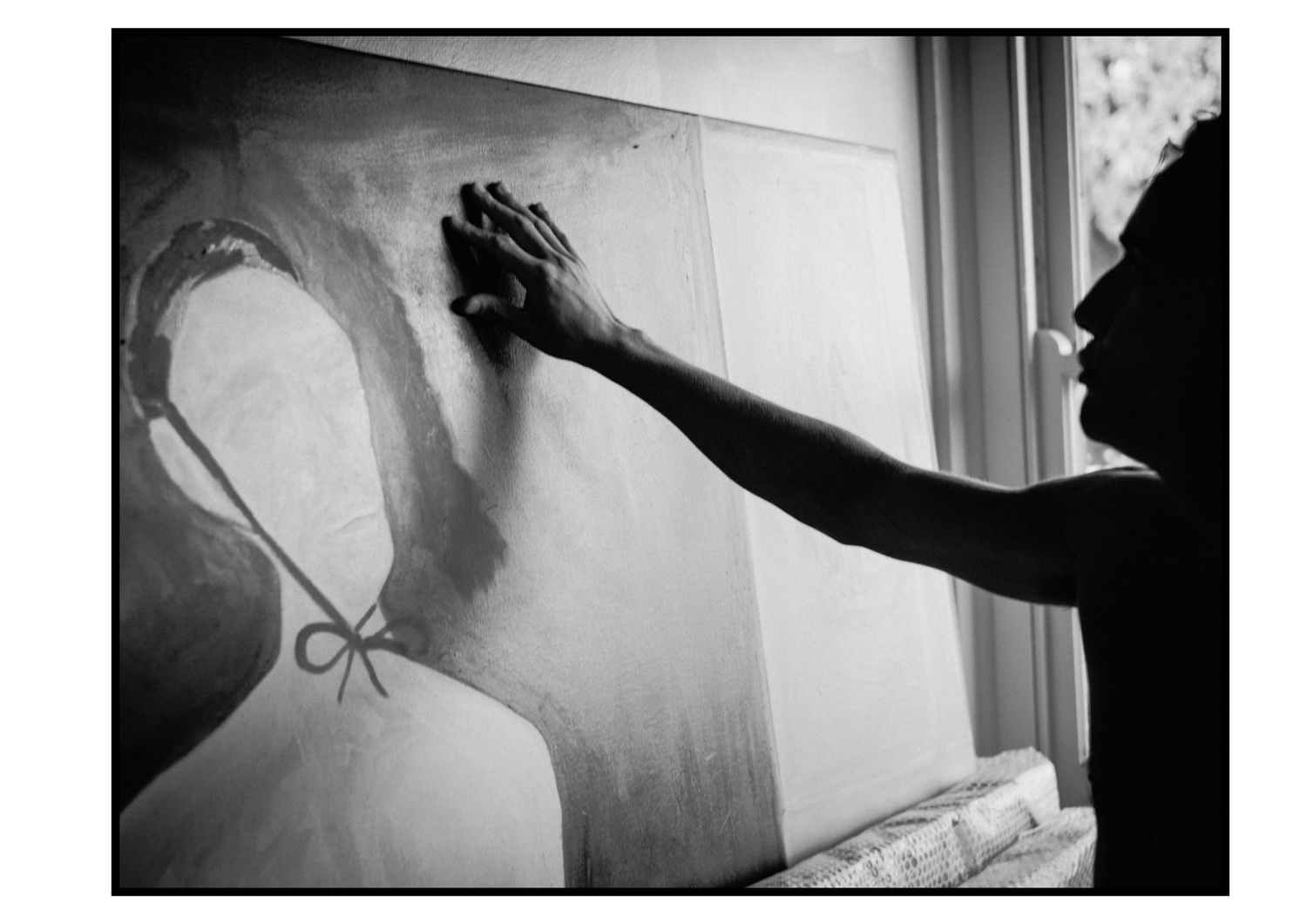 Artist's hand touching a large figurative painting near a window in black and white.
