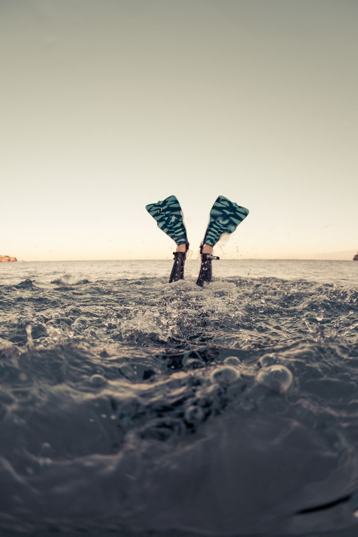Diver's fins sticking out of ocean water at sunset after diving in.