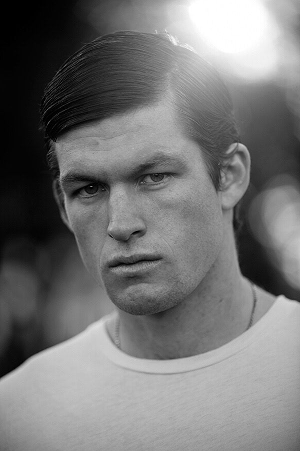Black and white portrait of young man with slicked hair wearing white t-shirt outdoors.